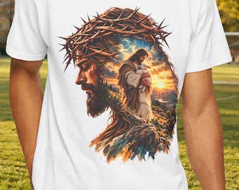 May include: A white short-sleeved t-shirt featuring a graphic print of a profile view of a bearded figure wearing a crown of thorns, with a smaller scene of a figure holding a lamb against a sunset landscape integrated within the design.