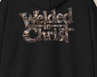 May include: A black hooded sweatshirt featuring the text "Welded in Christ" printed on the back. The lettering has a metallic, industrial appearance with visible weld marks and a dark, textured finish across the letters.