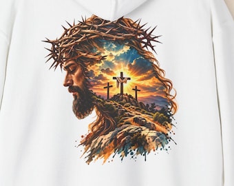 May include: A white hooded sweatshirt featuring a graphic print on the back. The design depicts a profile view of a bearded figure wearing a crown of thorns, set against a landscape with three crosses under a vibrant, sunlit sky.