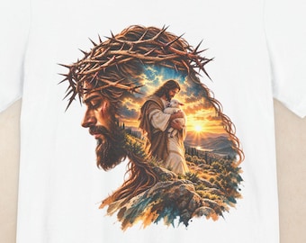 May include: A white t-shirt featuring a graphic print of a bearded figure wearing a crown of thorns. Inside the silhouette of the head, a smaller scene depicts a person holding a lamb against a sunset landscape with mountains and clouds.