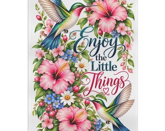 May include: A rectangular decorative towel featuring two hummingbirds with iridescent green and blue feathers, surrounded by pink hibiscus and small blue flowers. The text "Enjoy the Little Things" is printed in the center in dark blue and red script.
