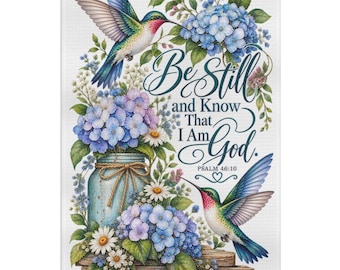 May include: A rectangular decorative towel featuring two hummingbirds, blue and purple hydrangea flowers, and a mason jar. The text reads Be Still and Know That I Am God. PSALM 46:10. The design includes green leaves and small white daisy-like flowers.