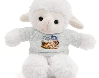 May include: A white plush lamb toy wearing a heather gray t-shirt. The shirt features a colorful graphic of a lamb lying in a manger under a bright star with the text The Bethlehem Journey 2026 printed above the image in a dark script font.
