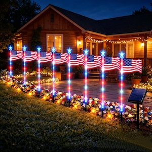 May include: A nighttime outdoor scene features a row of illuminated American flags. Each flag is mounted on a pole with red, white, and blue lights. A solar panel is visible in the foreground. The scene is set in front of a house with warm lighting.