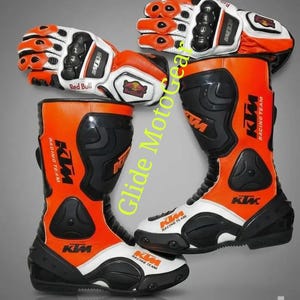 Könnte beinhalten: Orange und schwarze Motorradstiefel und -handschuhe. Die Stiefel und Handschuhe haben weiße Akzente und das KTM Racing Team-Logo. Die Handschuhe tragen auch das Red Bull-Logo. Der Text "Glide MotoGear" ist sichtbar.