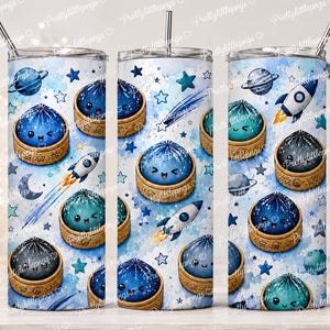 May include: A set of three stainless steel tumblers with space-themed designs. Each tumbler features illustrations of planets, rockets, stars, and smiling space creatures in shades of blue, teal, and gray. The tumblers have a silver straw.