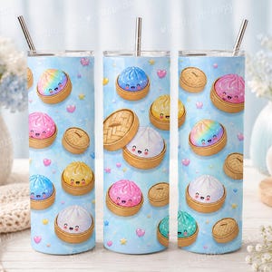Könnte beinhalten: Drei Edelstahlbecher mit einem skurrilen Design. Jeder Becher hat einen hellblauen Hintergrund, der mit lächelnden Cartoon-Knödeln in verschiedenen Farben, Herzen und Sternen verziert ist. Die Becher enthalten einen silbernen Strohhalm.