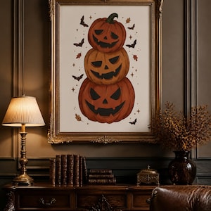 Peut inclure: Une impression d'art encadrée représentant une pile verticale de trois citrouilles d'Halloween orange aux visages sculptés. L'illustration est décorée de petites chauves-souris noires, de feuilles d'automne et d'étoiles sur fond blanc.