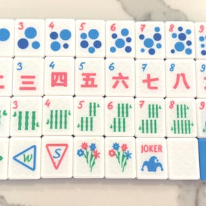 May include: A set of white Mahjong tiles with various symbols and numbers in red, green, and blue. The tiles feature dots, lines, and Chinese characters. One tile reads "JOKER".