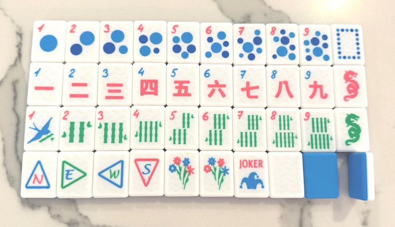 May include: A set of white Mahjong tiles with various symbols and numbers in red, green, and blue. The tiles feature dots, lines, and Chinese characters. One tile reads "JOKER".