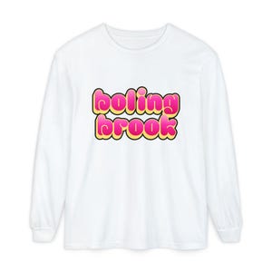 Pode incluir: Camiseta branca de manga comprida com o texto "boling brook" em letras rosa e amarelas. A camiseta tem gola redonda e mangas compridas. O texto está centralizado na frente da peça.