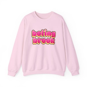 Pode incluir: Camisola rosa claro com o texto "boling brook" em fonte de bolhas. O texto é rosa com contorno amarelo e borda preta. A camisola tem mangas compridas e gola redonda.