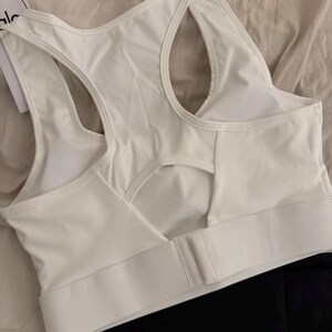 May include: White sports bra with a racerback design and a keyhole cutout in the back. The bra has a wide band under the bust and a hook-and-eye closure. The brand name "alo" is visible on a tag.