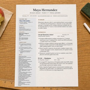 May include: A resume titled "Maya Hernandez" lies on a wooden surface, accompanied by a partially eaten red apple on a napkin, a ruler, a chalkboard eraser, and a piece of chalk. The resume details her experience as an educator.