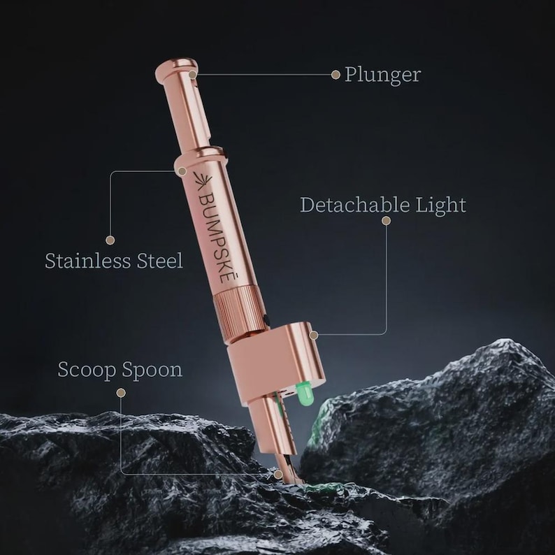 May include: A rose gold stainless steel tool labeled BUMPSKE featuring a plunger mechanism, a detachable light, and a scoop spoon. The device is positioned vertically with clear text labels pointing to its specific functional components.