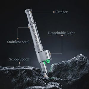 May include: A silver stainless steel BUMPSKE tool featuring a plunger mechanism at the top, a scoop spoon at the base, and a detachable light component. The device is labeled with the text BUMPSKE and includes lines pointing to its features.