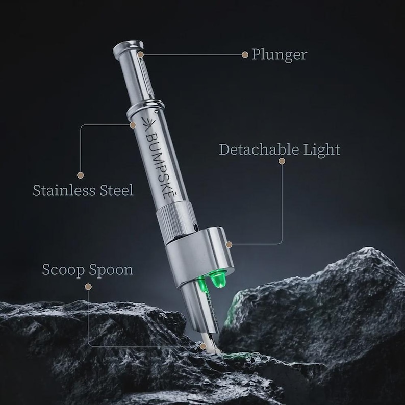 May include: A silver stainless steel BUMPSKE tool featuring a plunger mechanism at the top, a scoop spoon at the base, and a detachable light component. The device is labeled with the text BUMPSKE and includes lines pointing to its features.