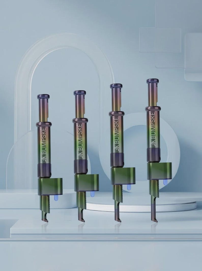 May include: Four vertical metal tools with an iridescent finish that shifts between purple, green, and gold. Each tool features the word BUMPSKE printed in white on the cylindrical body, a plunger-style top, and a small blue component at the base.