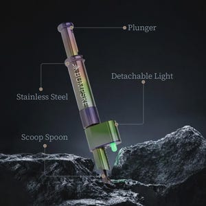 May include: A stainless steel tool with an iridescent finish featuring the text BUMPSKE. The device includes a plunger mechanism, a scoop spoon at the base, and a detachable light component that emits a small green glow from the side.