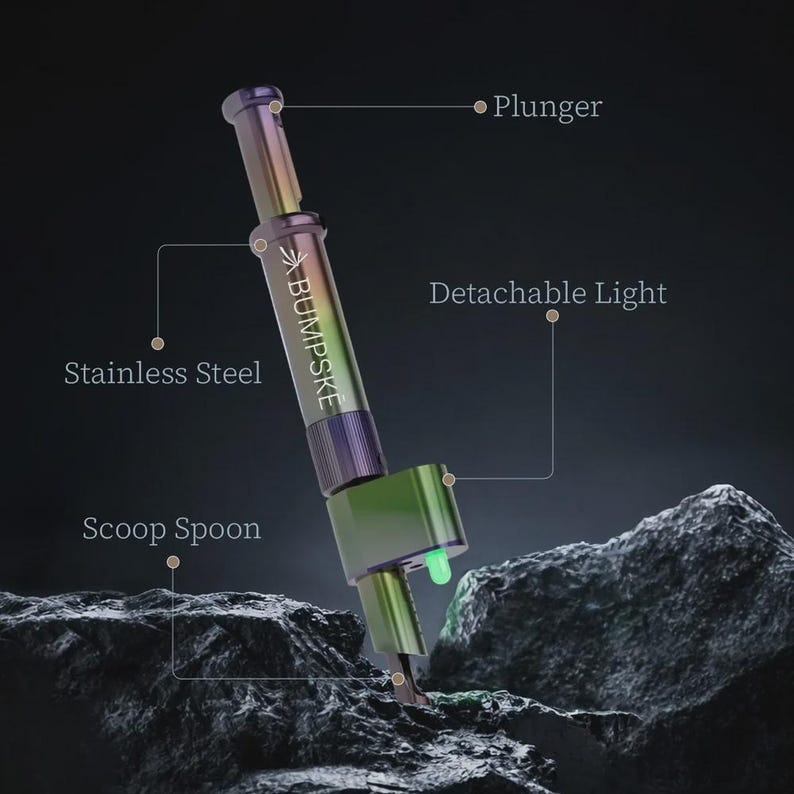 May include: A stainless steel tool with an iridescent finish featuring the text BUMPSKE. The device includes a plunger mechanism, a scoop spoon at the base, and a detachable light component that emits a small green glow from the side.