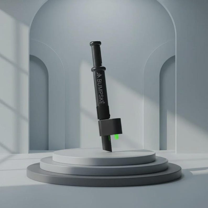 May include: A black cylindrical handheld device featuring the white text BUMPSKE printed vertically on its side. The tool has a plunger-style top, a central grip section, and a lower attachment with a small, bright green accent visible at the base.