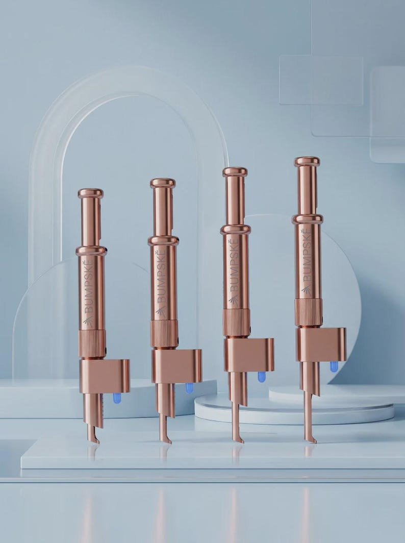 May include: Four rose gold metal devices arranged in a row, each featuring a cylindrical body with a plunger top, a textured grip section, and a side-mounted component with a small blue tip. The word BUMPSKE is engraved vertically on each unit.