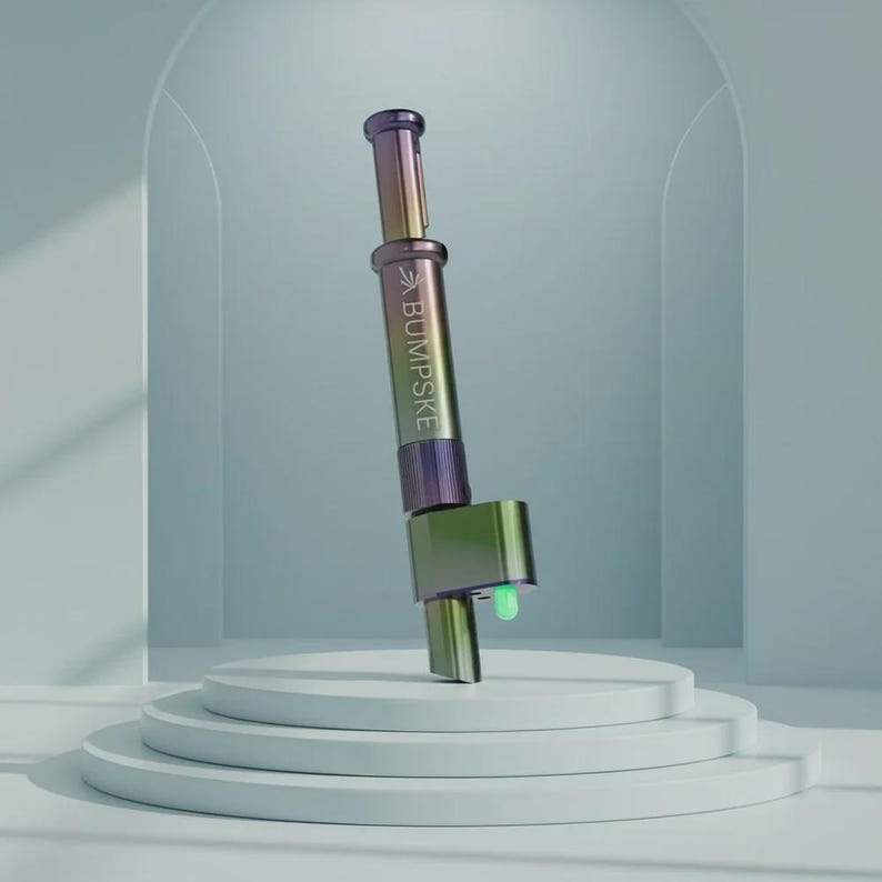 May include: A cylindrical metal tool with an iridescent finish that shifts between purple, green, and gold. The body features the text BUMPSKE printed vertically. It has a plunger mechanism at the top and a small, glowing green light at the base.