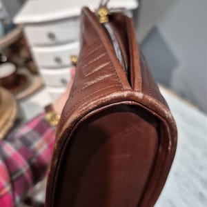 Pu&ograve; includere: Una borsa in pelle marrone con un design trapuntato. La borsa ha una chiusura a cerniera e finiture color oro. I bordi mostrano segni di usura.