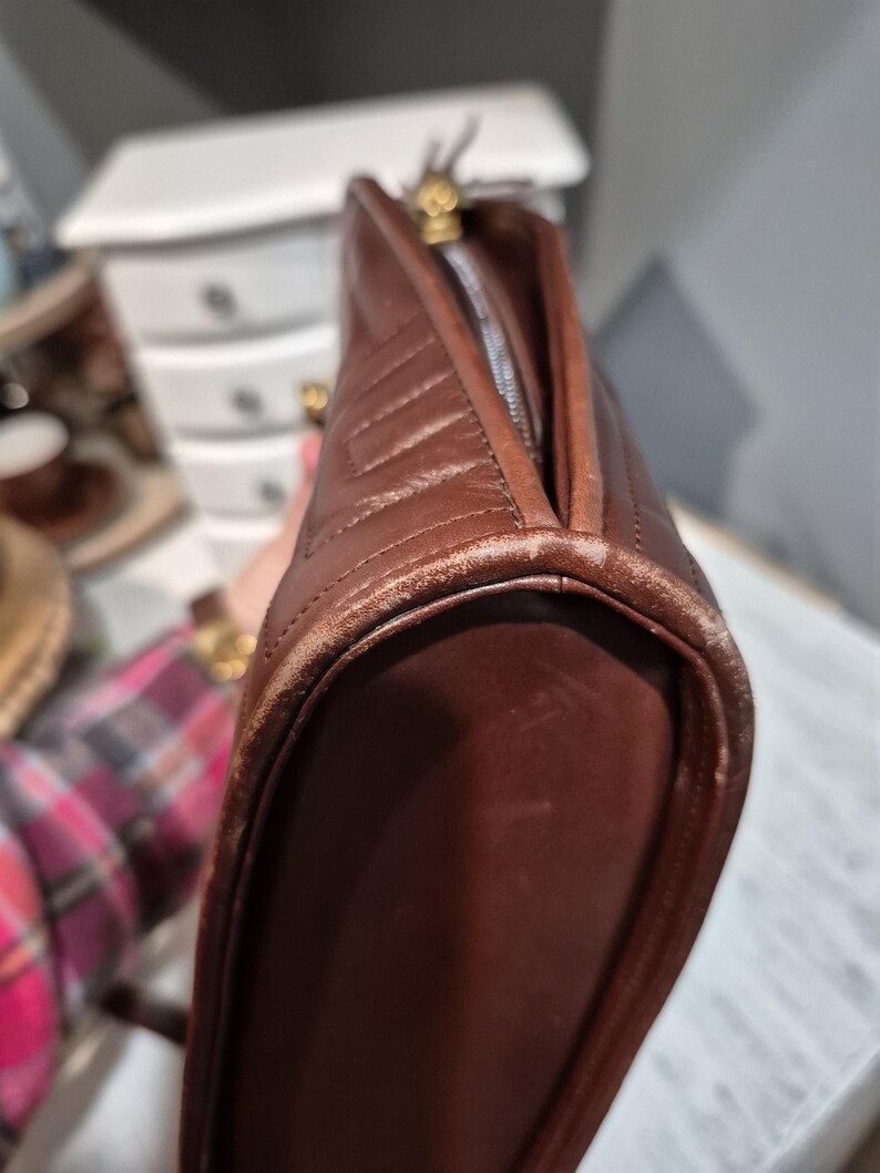Pu&ograve; includere: Una borsa in pelle marrone con un design trapuntato. La borsa ha una chiusura a cerniera e finiture color oro. I bordi mostrano segni di usura.