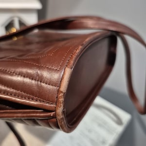 Pu&ograve; includere: Primo piano di una borsa in pelle marrone con un design trapuntato. La borsa ha una tracolla e mostra segni di usura sui bordi. La pelle &egrave; di un ricco e caldo colore marrone.