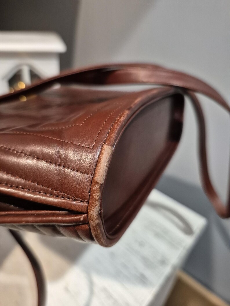 Pu&ograve; includere: Primo piano di una borsa in pelle marrone con un design trapuntato. La borsa ha una tracolla e mostra segni di usura sui bordi. La pelle &egrave; di un ricco e caldo colore marrone.