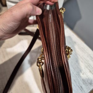 Pu&ograve; includere: Una borsa a tracolla in pelle marrone con catena dorata e chiusura a zip. La borsa &egrave; di un ricco colore marrone scuro e sembra essere realizzata in pelle di alta qualit&agrave;. La catena dorata aggiunge un tocco di eleganza.
