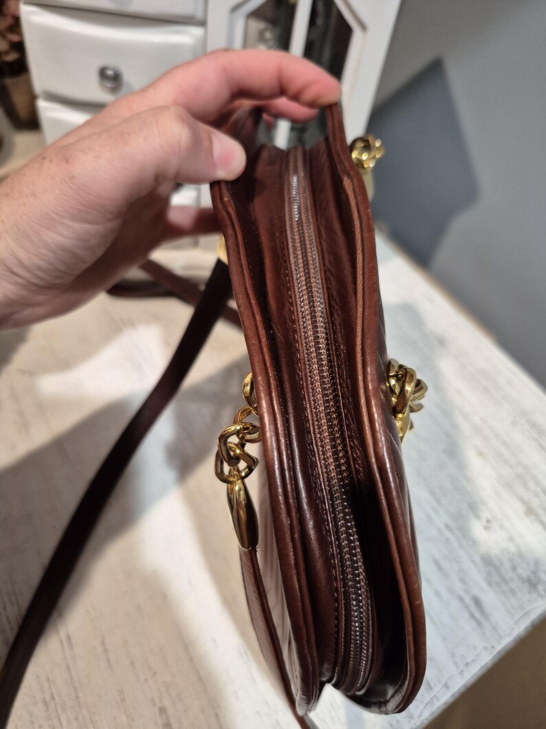 Pu&ograve; includere: Una borsa a tracolla in pelle marrone con catena dorata e chiusura a zip. La borsa &egrave; di un ricco colore marrone scuro e sembra essere realizzata in pelle di alta qualit&agrave;. La catena dorata aggiunge un tocco di eleganza.