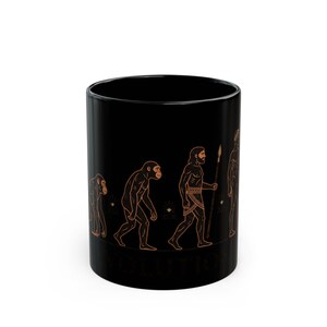 May include: A black ceramic mug featuring a linear graphic in orange and gold tones that depicts the stages of human evolution, starting from a primate and progressing to a human figure holding a spear, with the word EVOLUTION printed below.