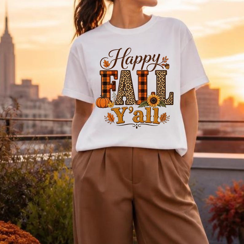 May include: A white short-sleeve t-shirt featuring the text Happy Fall Y'all in black and orange. The letters are filled with orange and black plaid and leopard print patterns, accented by a pumpkin, a sunflower, and autumn leaves.