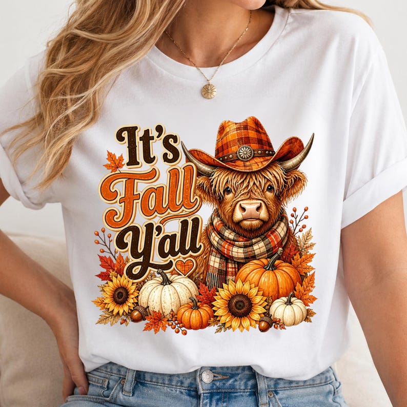 May include: A white t-shirt featuring a graphic of a Highland cow wearing a plaid cowboy hat and scarf. The text reads It's Fall Y'all. The design includes orange and white pumpkins, sunflowers, and autumn leaves in shades of orange and brown.