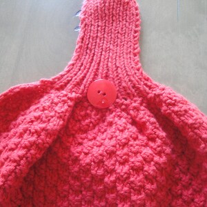 May include: A close-up of a red knitted fabric with a red button in the center.