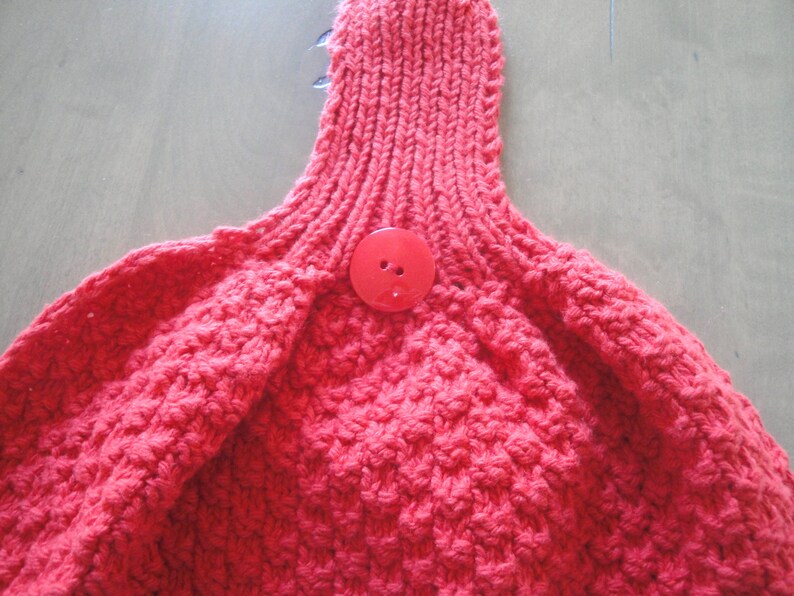 May include: A close-up of a red knitted fabric with a red button in the center.