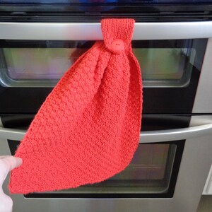 May include: A red knitted oven mitt with a button on the top, hanging on a silver oven door.