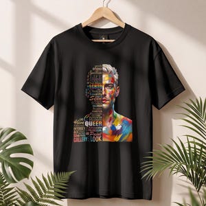 Könnte beinhalten: Ein schwarzes Kurzarm-T-Shirt mit einem Grafikdruck eines in zwei Hälften geteilten Gesichts. Eine Seite besteht aus buntem Text mit Wörtern wie LGBTQ, Queer und Equality, während die andere Seite ein realistisches Gesicht mit bunten Farbstrichen zeigt.
