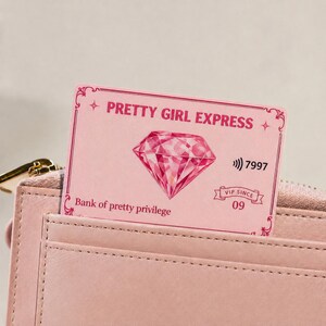 May include: A pink card with the text "PRETTY GIRL EXPRESS" and a diamond graphic. The card also has the text "Bank of pretty privilege", "7997", and "VIP SINCE 09". The card is partially visible in a pink leather wallet.