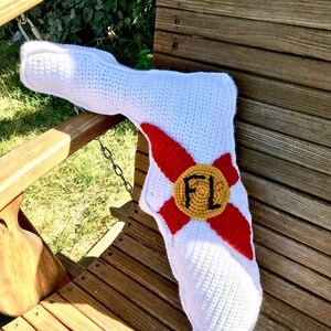 Puede incluir: Almohada de crochet blanco con forma del estado de Florida con un emblema del estado de Florida de crochet rojo y amarillo con las letras "FL" en el centro.