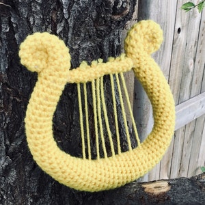 Op de afbeelding: Een gele gehaakte harp tegen een houten achtergrond.
