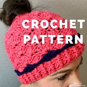 May include: A pink crochet hat with a navy blue trim. The hat is designed to be worn with a bun. The text "CROCHET PATTERN" is superimposed on the image.