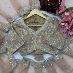 Puede incluir: Un conjunto de blusa y falda en color melocot&oacute;n claro con intrincados bordados plateados en un patr&oacute;n de cuadr&iacute;cula de diamantes. La blusa tiene mangas cortas y cuello en V, mientras que la falda es de tela plisada transparente con detalles de lentejuelas plateadas.