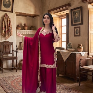 Könnte beinhalten: Ein tief magentafarbenes Salwar-Kameez-Set, bestehend aus einer langärmeligen Tunika mit Rundhalsausschnitt und einer passenden weiten Hose. Das Kleidungsstück ist mit cremefarbener Blumenstickerei am Ausschnitt, an den Ärmelbündchen und am Saum verziert und wird durch einen passenden magentafarbenen Dupatta mit cremefarbener Spitzenborte ergänzt.