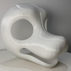 May include: A white, smooth, three-dimensional animal-shaped mask base featuring a rounded cranium, a prominent snout, and large, circular eye openings. The structure is hollow with an open mouth area and a glossy, uniform finish throughout.