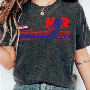 K&ouml;nnte beinhalten: Dunkelgraues T-Shirt mit einem grafischen Design mit dem Text "H&R" in Rot, einem blau-roten Design, der kroatischen Flagge und den Worten "CROATIA SOCCER" und "WORLD CUP '16".