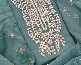 May include: A sage green fabric garment featuring an intricate central panel of silver-toned leaf-shaped embroidery. The surrounding fabric is adorned with scattered, delicate silver-toned floral motifs connected by thin, metallic silver threads.