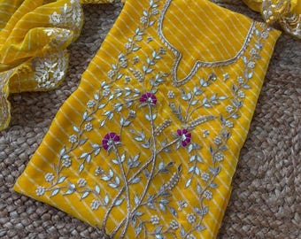 May include: A bright yellow fabric garment featuring thin white horizontal stripes and intricate embroidery. The design includes silver-toned leaf-shaped embellishments, small white beads, and vibrant magenta floral accents arranged in a central pattern.